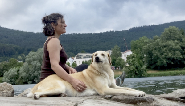 Gemma Mari Gurt mit ihrem Hund auf einem Stein sitzend am Neckar